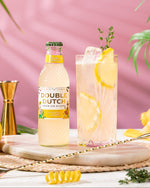 Double Dutch Double Lemon bottle with a glass of lemonade on a pink background