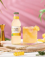 Double Dutch Double Lemon bottle with a glass on a wooden board against a pink background