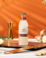 Bottle of Double Dutch ginger beer on a wooden board with ginger and lime, against an orange background.
