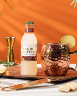Bottle of Double Dutch ginger beer with a copper mug and ingredients on an orange background