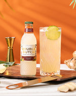 Bottle of Double Dutch Ginger Beer with a glass of ginger beer on a wooden board against an orange background.