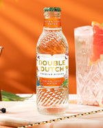 Double Dutch Indian Tonic Water bottle with a cocktail and grapefruit on an orange background