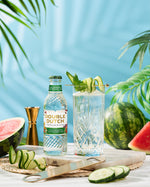 Double Dutch Cucumber and watermelon bottle with a cocktail and watermelon slices on a table with a blue background